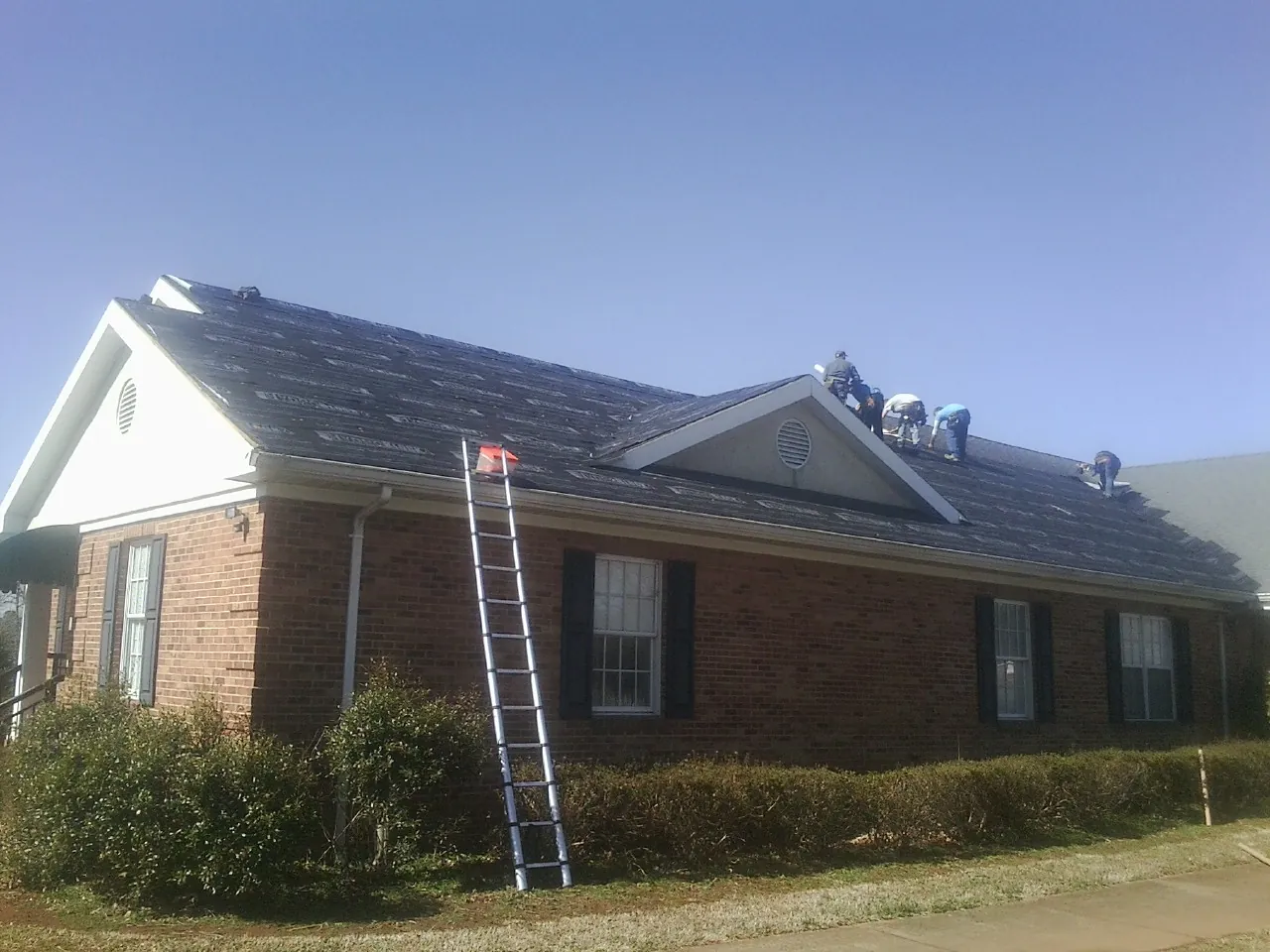 Crew tearing shingles off a brick ranch roof with a ladder set — Emergency Roof Repair work by our crew in South San Francisco