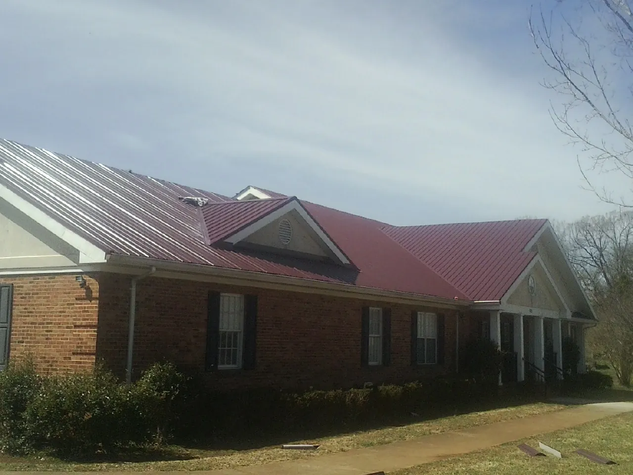 Red metal roof with gabled entries on a long brick building, from a Hail Damage Roof Repair job in South San Francisco