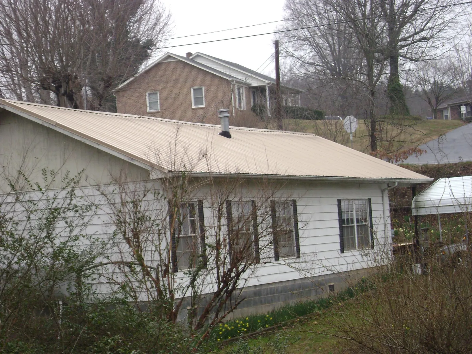 Tan metal roof on a white sided house set into a hillside — Commercial Roofing by Roofing Brothers in South San Francisco